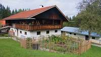 Ein altes Bauerhaus mit einem Balkon aus Holz, davor ist ein Kräutergarten. 