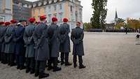 Soldatinnen und Soldaten stehen in Formation angetreten vor einem Schloss mit gelb-weißer Fassade.