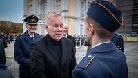 Ein blonder Mann schüttelt einem Soldaten die Hand und lächelt.