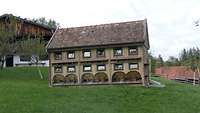 Ein riesiges Bienenhotel über 2 Stockwerke steht auf einer Wiese. 