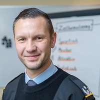 Oberstleutnant Niklas S. blickt in die Kamera, hinter ihm ist ein Flipchart aufgebaut