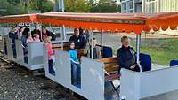 Kinder und Erwachsene sitzen in Anhängern einer Mini-Eisenbahn.