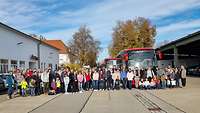 Mehrere Personen stehen bereit um mit 2 Bussen zu fahren. 