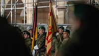 Mehrere Soldatinnen und Soldaten stehen in einer Formation. Zwischen ihnen sind zwei Fahnen.