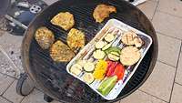 Auf einem Grill liegt Fleisch und Grillgemüse.