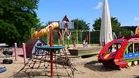 Auf einem Kinderspielplatz stehen diverse Spielgeräte wie Baumhaus, Klettergerüste und Schaukeln.