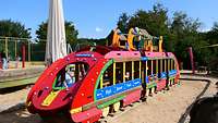 Ein großer, bunter Holzzug steht auf einem Sandspielplatz.