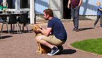 Ein Mann hockende vor einem Hund und kraulte dessen Kopf.
