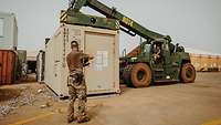 Ein Soldat nimmt mit einem Containerstapler einen Container auf. Ein Soldat gibt ihm Anweisungen.