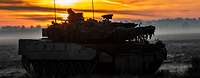 Auf einem Feld im Winter bei aufgehender Sonne steht ein Panzer.