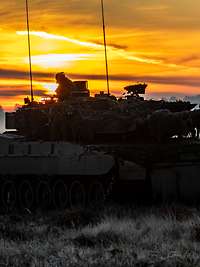 Auf einem Feld im Winter bei aufgehender Sonne steht ein Panzer.