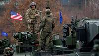 Drei Soldaten stehen auf einem amerikanischen Kampfpanzer und reden miteinander. 
