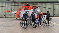 vier Rennradfahrer vor einem Hubschrauber