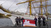 sechs Männer stehen vor dem Segelschulschiff Gorch Fock