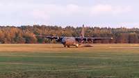 Eine C-130J setzt zur Landung auf einer Grasfläche an.