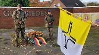 Eine Soldatin und ein Soldat stehen neben einem Kranz am Ehrenmal in Bethen