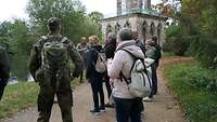 Eine Personengruppe und ein Soldat stehen vor einem antiken Gebäude.