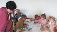 Einige Kinder malen und basteln mit einer Frau an einem Tisch.