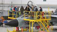 Einige Menschen stehen auf einem gelben Treppenaufgang und blicken ins Cockpit eines Tornados.