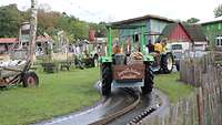 Ein Traktor fährt auf regennasser Fahrbahn auf ein Gebäude zu. 