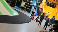 Erwachsene und Kleinkinder spielen in einer Halle auf einer gelben Rutsche.