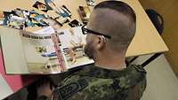Ein Soldat betrachtet eine Sammlung von Fotos und Zeitungsartikeln.