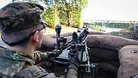 Ein Soldat schaut auf eine Straße. Er steht hinter Sandsäcken und hält eine Waffe.