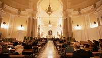 Viele Menschen sitzen auf Bänken in einer Kirche und hören dem Heeresmusikkorps zu.