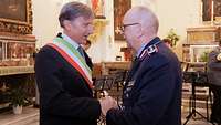 Ein Soldat gibt einem Mann die Hand. Der Mann trägt ein Band in den italienischen Landesfarben um den Körper.