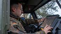 Soldat bedient ein Tablet im Fahrzeug sitzend. 