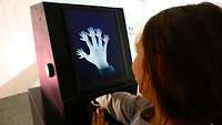 Ein Kind hält seine Hand in einen Apparat, aus jedem einzelnen Finger wuchs plötzlich eine Hand.
