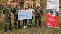Zwei Frauen und drei Soldaten stehen nebeneinander und halten einen Spendenscheck vor sich.
