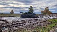 Ein getarnter Kampfpanzer vom Typ Leopard fährt durch ein schlammiges Gelände