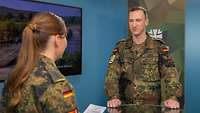 Eine Soldatin interviewt einen Soldaten vor einem Monitor.