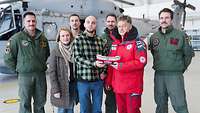 Mehrere Menschen stehen in einer Halle vor einem Hubschrauber mit einer Spendenkasse in der Hand.