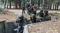 Soldaten laufen hintereinander in einen ausbetonierten, mit Windungen angelegten Graben.