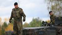 Ein Panzerkommamdat steht auf dem Heck seines Kampfpanzers und schaut zu seinen Kameraden hinunter. 