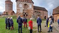 Mehrere Menschen stehen auf einem Burghof und lauschen den Ausführungen des Burgführers.