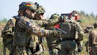 Zwei Soldaten üben mit der Pistole P8 auf einer Schießbahn, im Hintergrund weitere Soldaten.