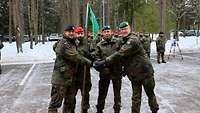 Drei Soldaten legen ihre Hände zur Mitte über Kreuz, ein vierter Soldat hält einen grünen Wimpel.