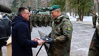 Ein Zivilist in blauer Jacke übergibt einem Soldaten ein schwarzes Kästchen mit Urkunde.