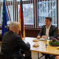 Zwei Männer und eine Frau sitzen sich am Tisch gegenüber.