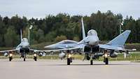 Three combat aircraft are taxiing on the runway of an airfield.