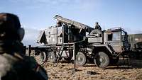 A soldier is standing on a truck and checking a large, rectangular radar that has already been erected.