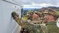 Drei Soldaten stehen vor der Seitenwand eines weißen Lastwagens und bewegen farbige Magnete.