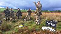 Ein britischer Soldat steht im Gelände vor vier weiteren Soldaten und erklärt etwas.