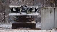 Ein Brückenlegepanzer Biber steht neben einer Betonmauer. 