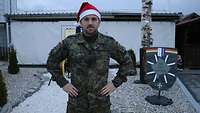 Ein Soldat mit Weihnachtsmütze steht vor einem Gebäude.