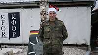 Eine Soldatin mit einer Weihnachtsmütze steht vor einem Gebäude.