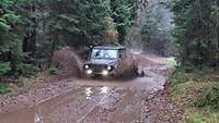 Ein Geländewagen fährt im Wald durch eine Pfütze.